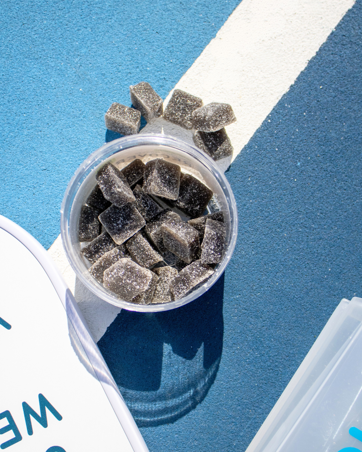 Clear container with dark gummies on a blue surface