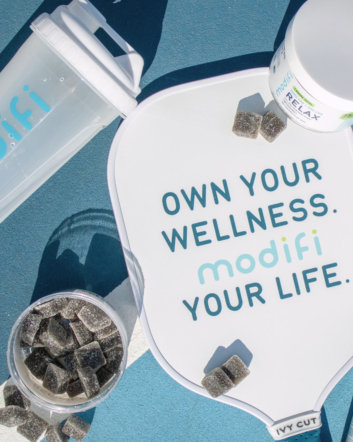 Modifi wellness products with text 'Own your wellness. modifi your life.' on a blue background