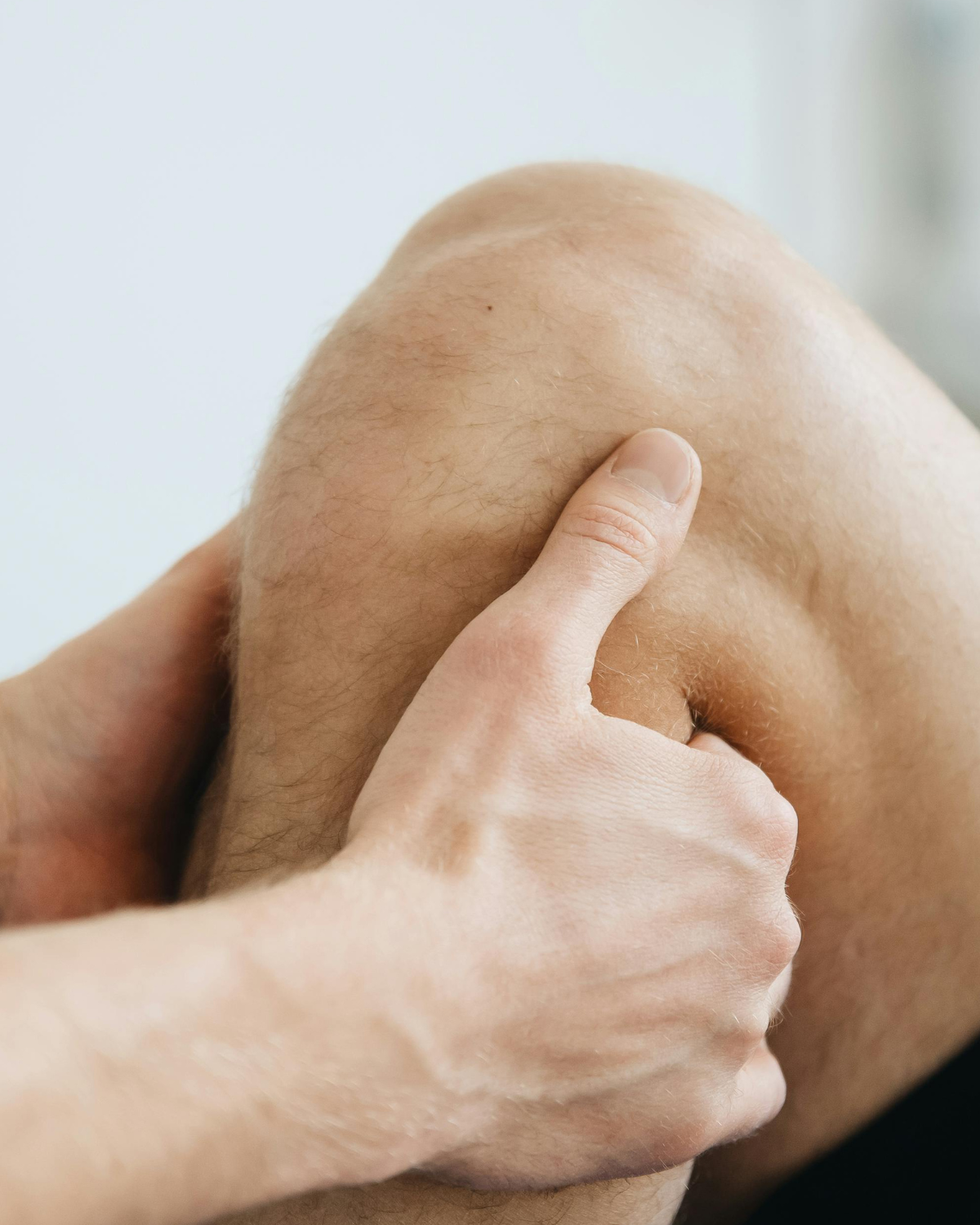 close up of a man holding his knee on a cream background