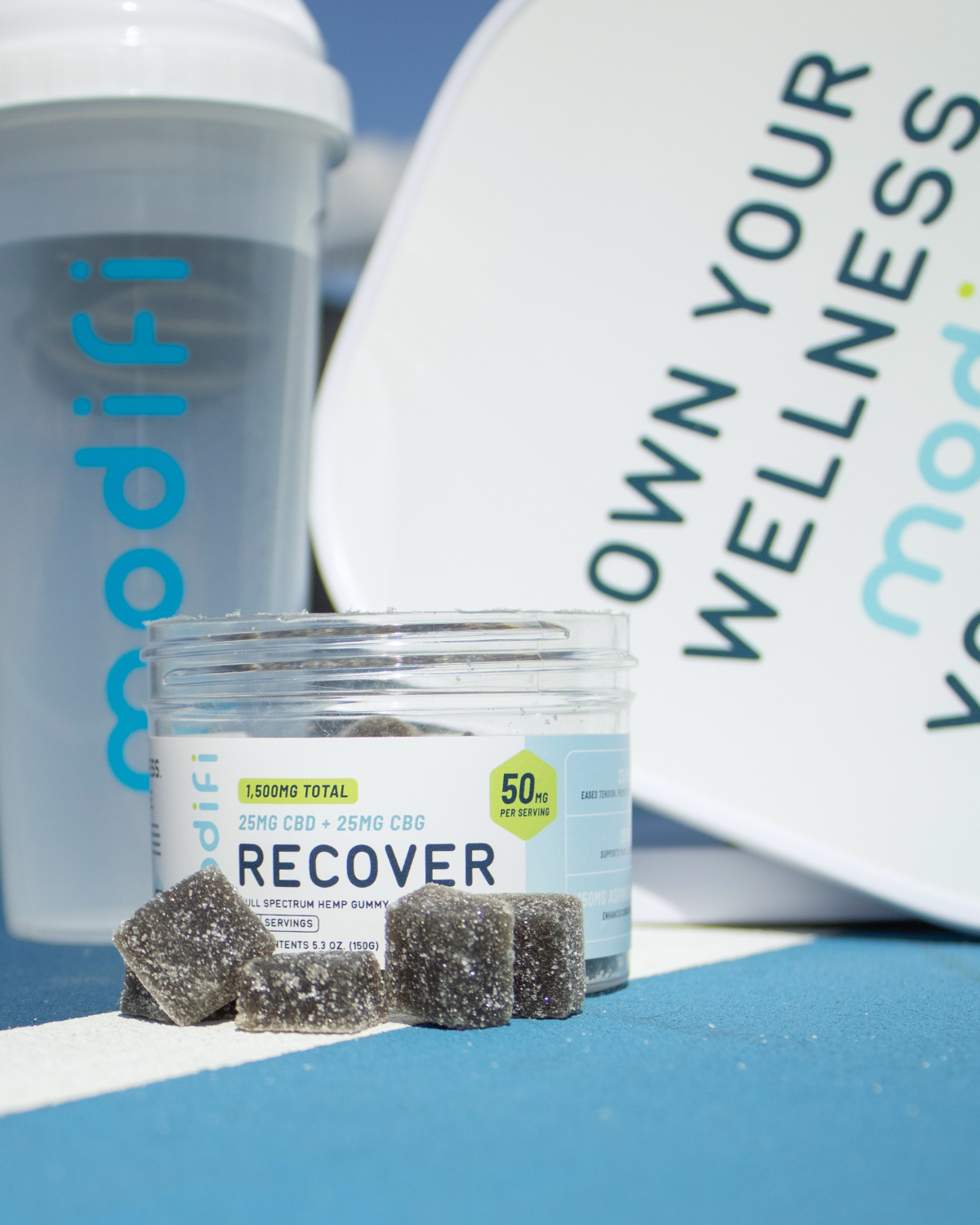 Modifi Recover supplement jar with gummies on a blue surface, with 'modifi' branding visible.